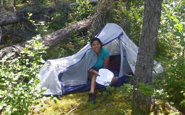 a student smiles from their shelter in a wooded area on an outward bound course